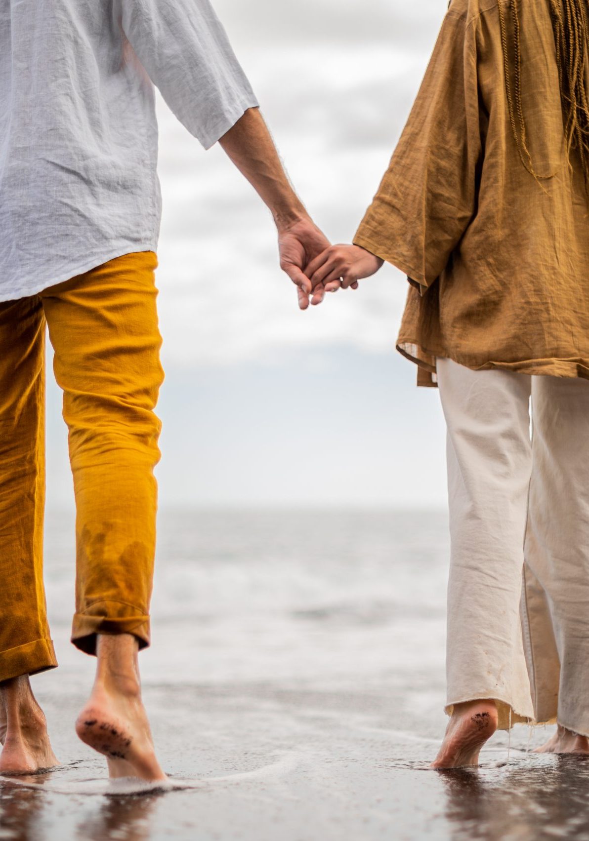 Young loving couple shown from behind holding hands on a beach. High quality photo. Cloudy weather.